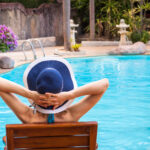 Frau mit Hut entspannt auf einer Liege am Pool