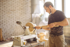 Junger Tischler, der Holzbretter auf einer speziellen Holzbearbeitungsmaschine verarbeitet