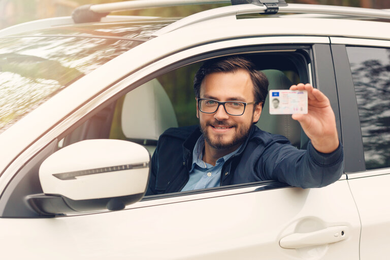 Ein junger glücklicher Mann zeigt seinen neuen Führerschein