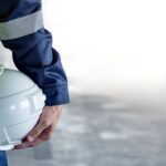 Mitarbeiter mit Sicherheitshelm und Warnweste zeigt professionelle Arbeitskleidung besticken fuer Handwerk und Industrie